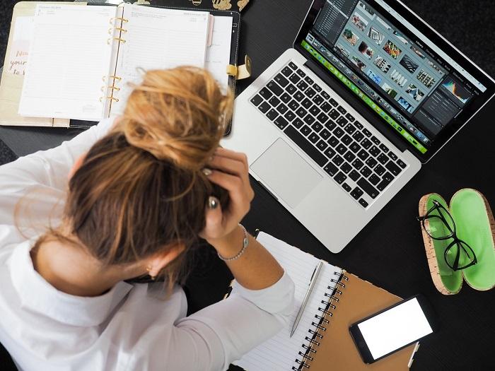 Ein Mädchen sitzt vor dem Laptop und vielen Notzibüchern und schlägt die Hände über dem Kopf zusammen: Zu viel Arbeit