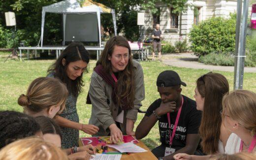 Eine Gruppe junger Menschen und zwei Workshopleitungen sitzen draußen und unterhalten sich angeregt.